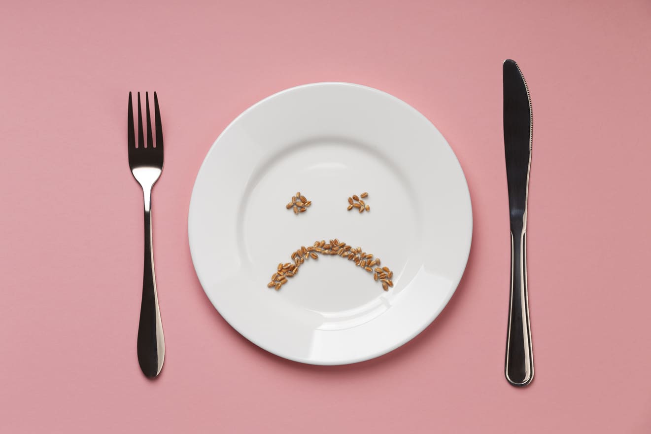 Empty plate with seeds arranged in sad face, illustrating hunger and digestive discomfort