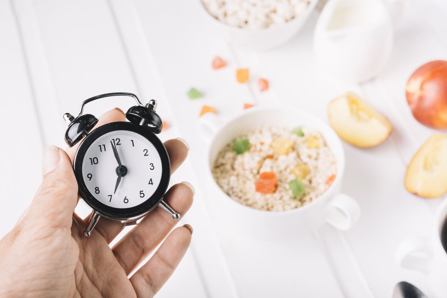 Hand holding alarm clock over breakfast