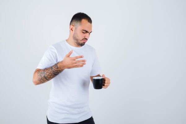 Man holding coffee cup while suffering from heartburn symptoms