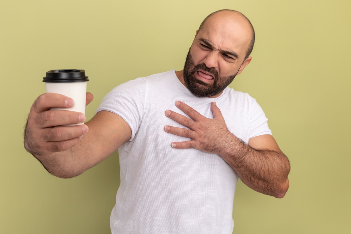 Man with heartburn looking at coffee cup with a disgusted look