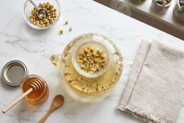 Glass teapot brewing chamomile tea with honey and spoon for acid reflux symptom relief