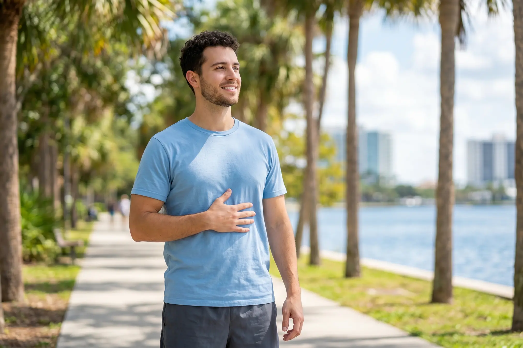 Smiling young man holding his stomach outdoors near the water.