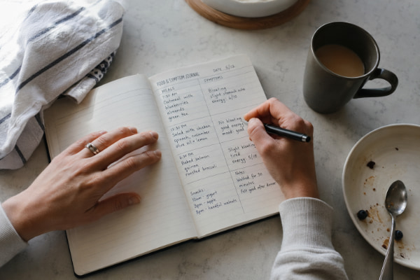 Person logging meals and heartburn in a food diary to find acid reflux triggers