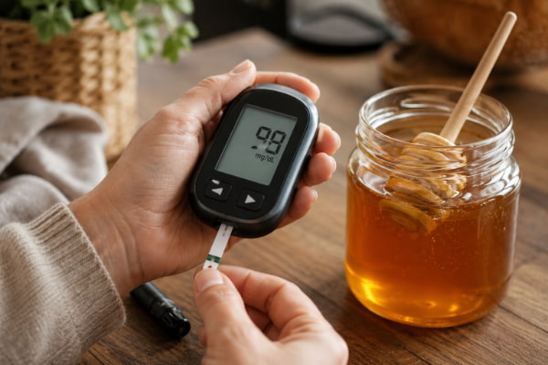 Glucose meter beside a honey jar, showing why honey needs caution with reflux and diabetes