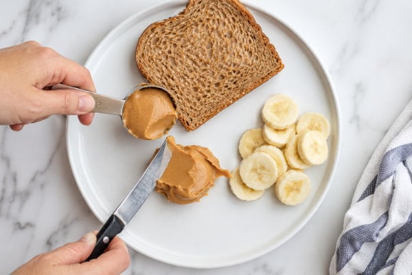 Level tablespoon of peanut butter measured onto plate with sliced banana