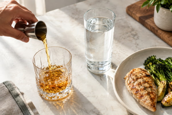 Measured whiskey pour next to water and a light meal to reduce acid reflux risk