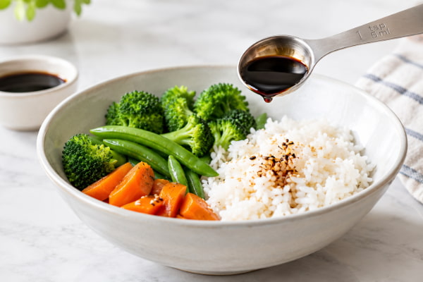 Measuring teaspoon of soy sauce over rice showing portion control for heartburn