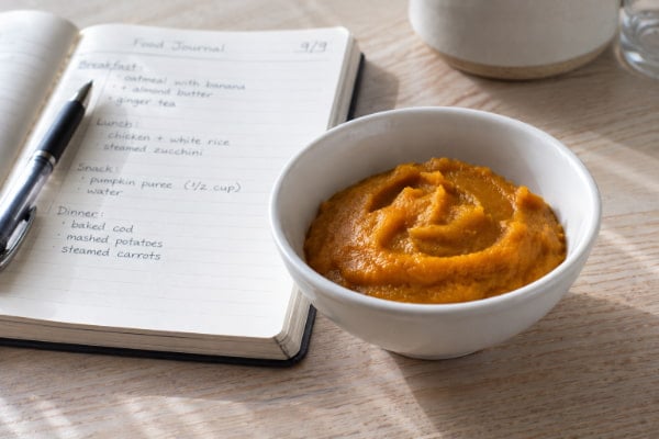 Half cup portion of plain pumpkin puree next to a food diary used to test reflux triggers