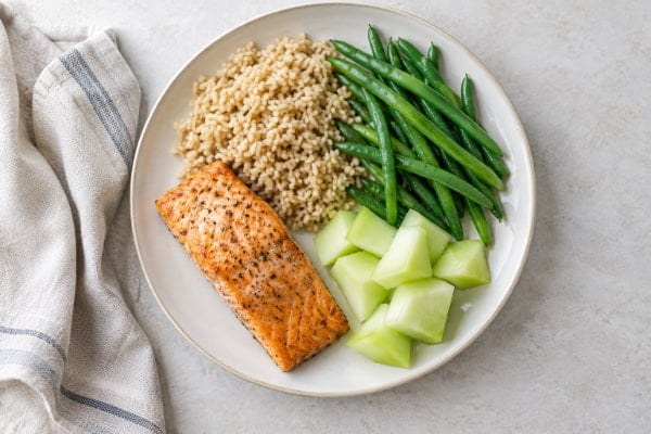 Reflux-friendly plate with baked salmon, brown rice, melon and steamed vegetables