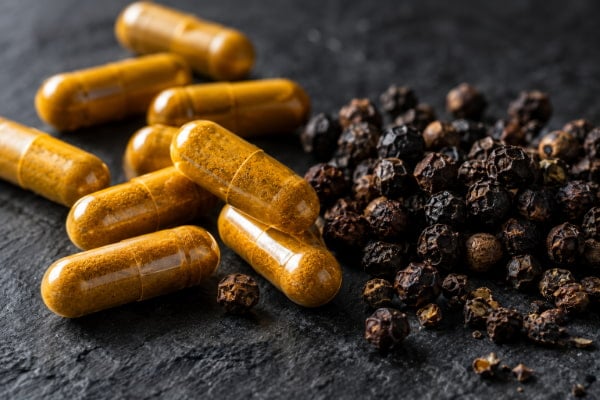 Turmeric capsules beside black peppercorns, the piperine pairing linked to higher risk in reflux patients