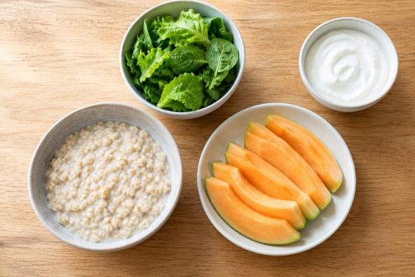 Oats, melon and leafy greens on a table as low-acid foods that help prevent heartburn
